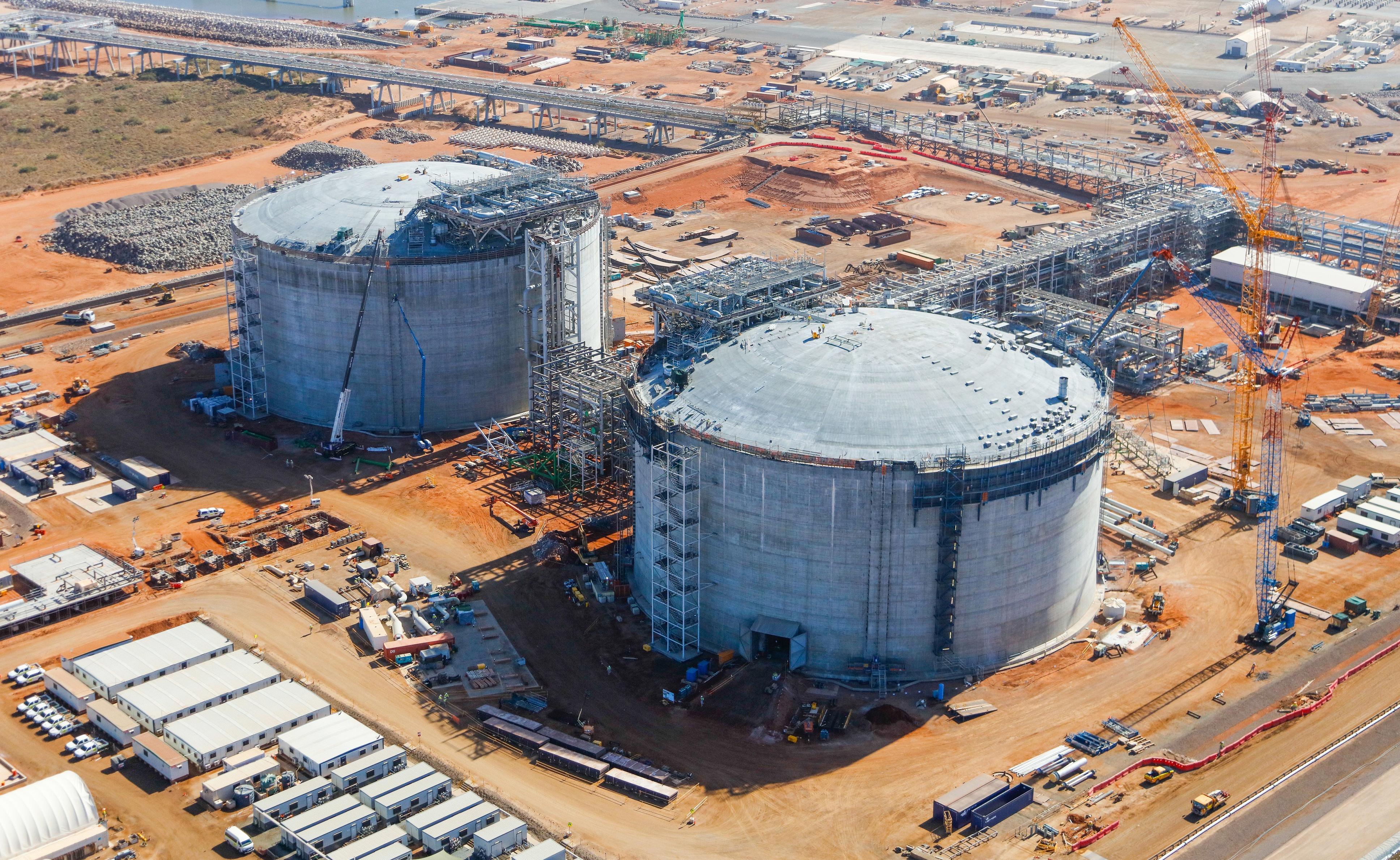 This is an aerial photograph of the Wheatstone Liquefied Natural Gas Plant, focused on the two large tanks surrounded by containers, portastations, and scaffolding.