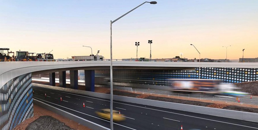 This is a photograph of the major project overpass over the freeway that Monford Group completed. The cars traveling underneath are blurred from the speed they are traveling. Artwork decorates the sides of the large infrastructure..