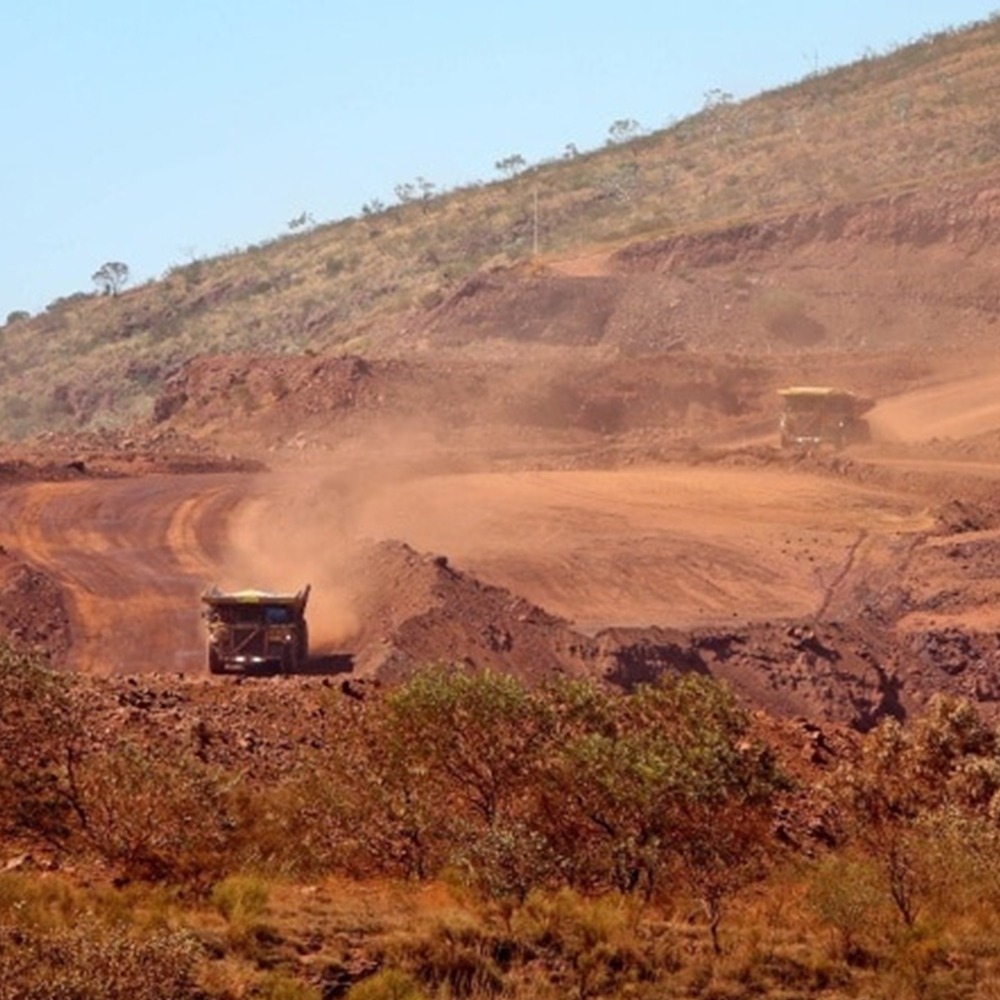 This photograph is of two large mining specific trucks descending into the main mining pit to be loaded with ore. The red dust from the trucks dissipates over the landscape.