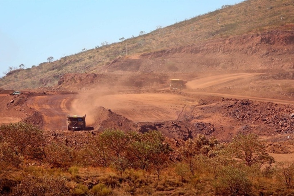 This photograph is of two large mining specific trucks descending into the main mining pit to be loaded with ore. The red dust from the trucks rises dissipates over the landscape.